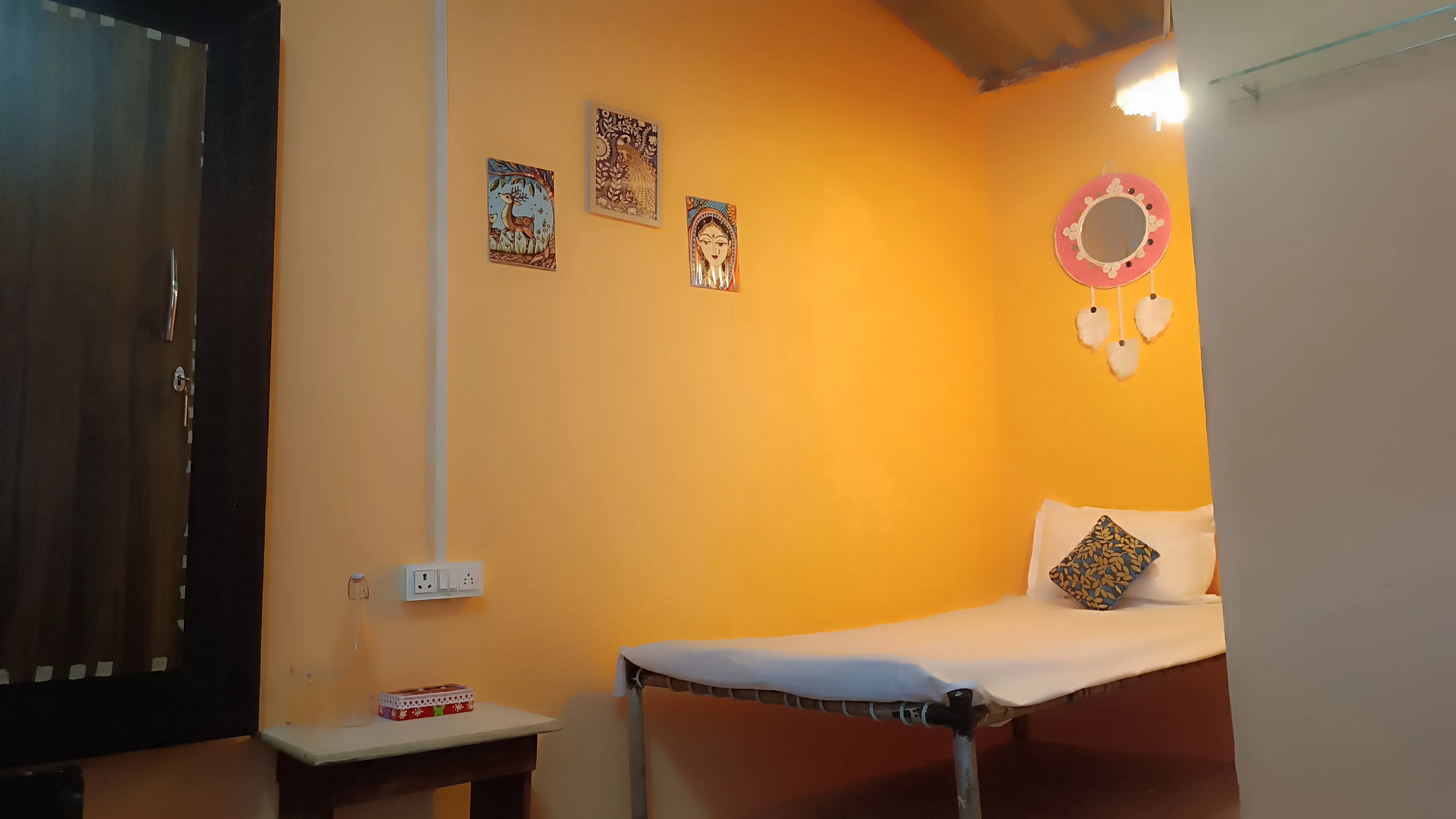 Inside the single hut, with a charpai, mirror and wall decorations.